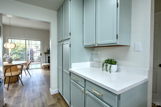 kitchen featuring light wood finished floors, decorative light fixtures, a fireplace, light countertops, and baseboards