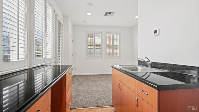 kitchen with sink, light colored carpet, and dark stone counters