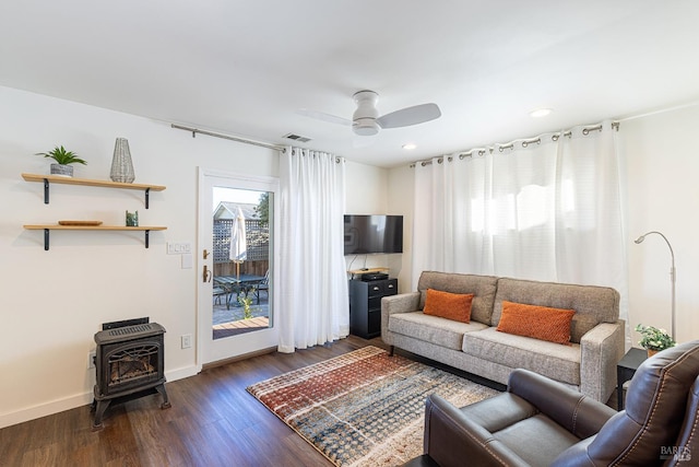 living room with dark wood finished floors, visible vents, a ceiling fan, a wood stove, and baseboards