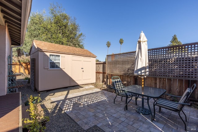 view of patio featuring a storage shed, outdoor dining space, fence, and an outbuilding