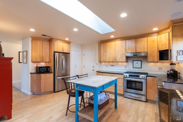 kitchen with under cabinet range hood, tasteful backsplash, a skylight, and appliances with stainless steel finishes