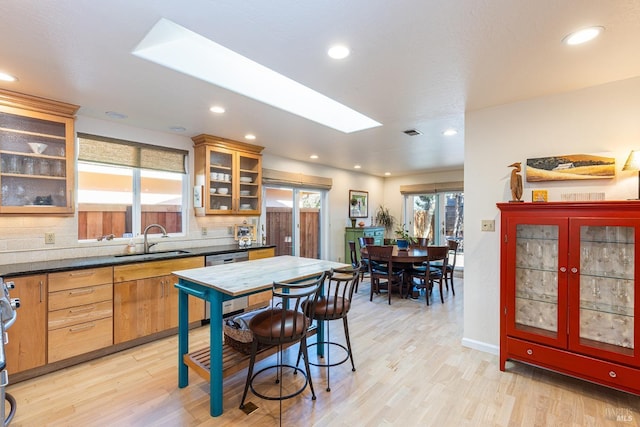 kitchen with backsplash, dark countertops, a sink, and light wood-style floors