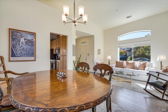 dining room with an inviting chandelier, wood-type flooring, and high vaulted ceiling