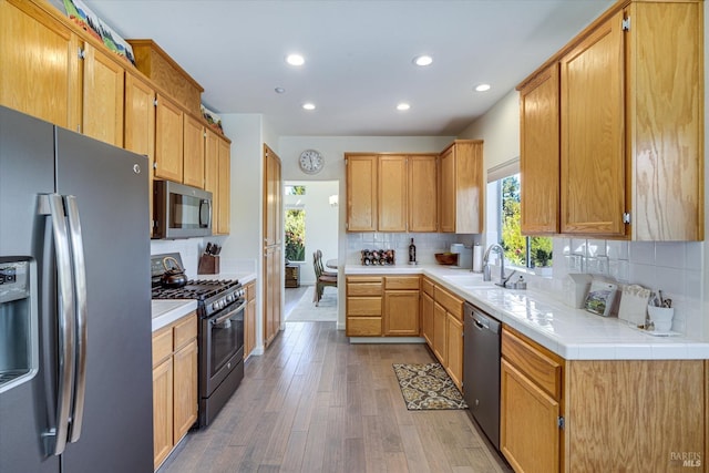 kitchen featuring sink, wood-type flooring, tile counters, stainless steel appliances, and backsplash