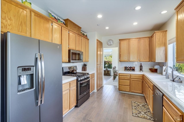 kitchen with sink, tile countertops, light hardwood / wood-style flooring, appliances with stainless steel finishes, and backsplash