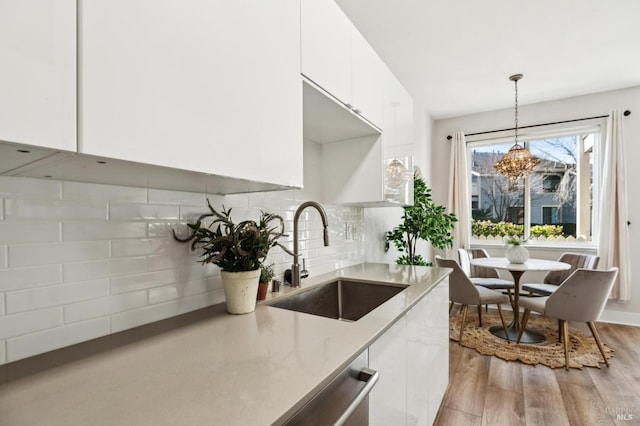 kitchen with pendant lighting, sink, white cabinets, decorative backsplash, and light wood-type flooring