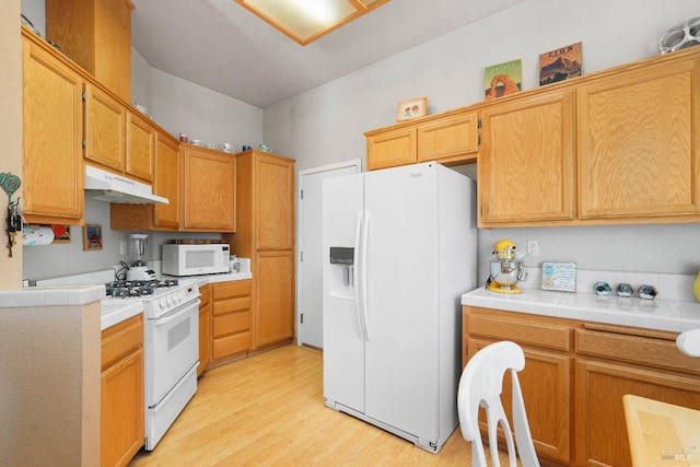 kitchen featuring light wood-type flooring, tile countertops, and white appliances