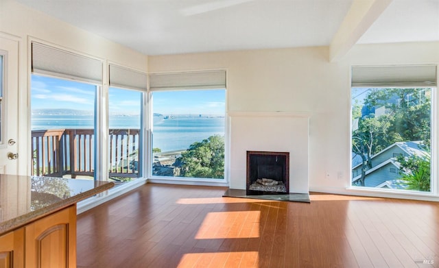 unfurnished living room featuring a water view, plenty of natural light, and dark hardwood / wood-style floors