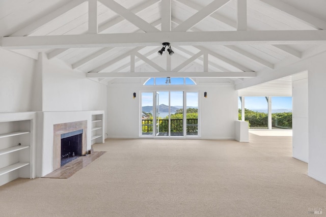 unfurnished living room with beam ceiling, a fireplace, light carpet, a mountain view, and built in shelves