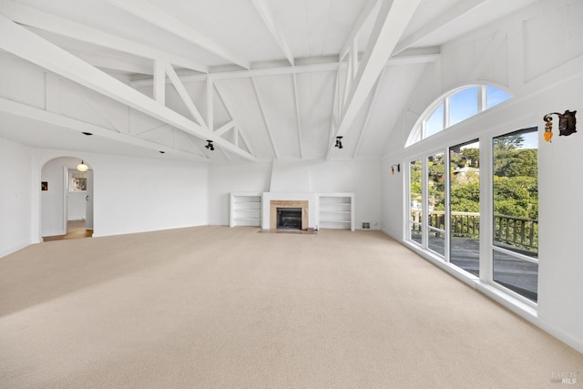 unfurnished living room featuring a tiled fireplace, carpet, high vaulted ceiling, and beamed ceiling