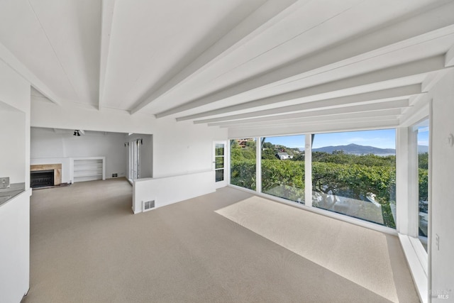 unfurnished room featuring beamed ceiling, a mountain view, carpet floors, and a wealth of natural light