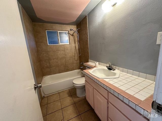 full bathroom with tiled shower / bath combo, vanity, tile patterned flooring, toilet, and a textured ceiling