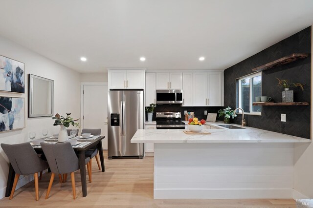 kitchen with appliances with stainless steel finishes, sink, white cabinets, and light stone counters