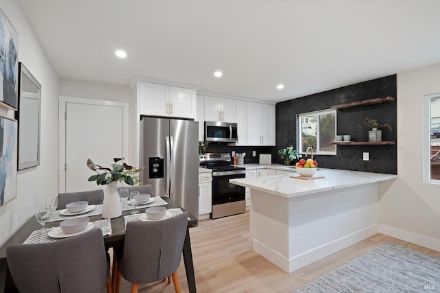 kitchen with stainless steel appliances, light hardwood / wood-style floors, light stone countertops, white cabinets, and kitchen peninsula