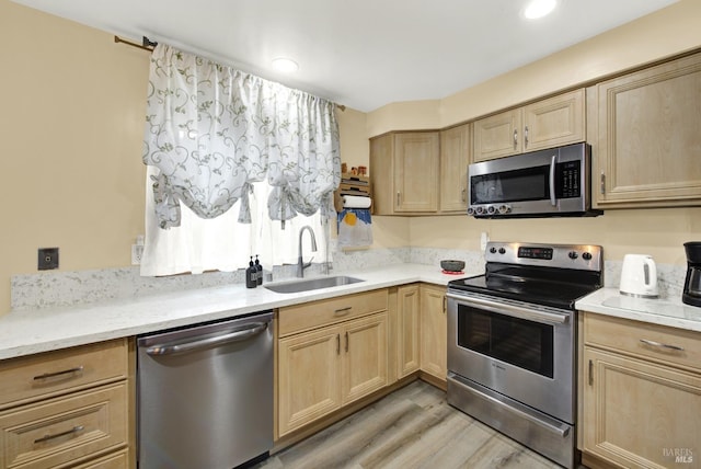 kitchen with appliances with stainless steel finishes, light brown cabinetry, sink, and light wood-type flooring