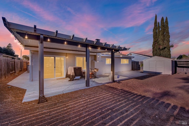 back house at dusk featuring a shed and a patio area