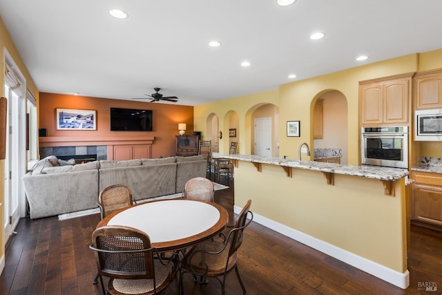 dining space with a fireplace, dark wood-type flooring, sink, and ceiling fan