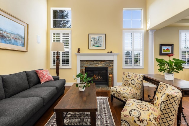 living room with wood-type flooring, a stone fireplace, decorative columns, and a high ceiling