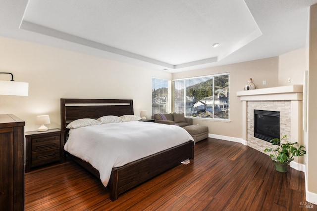 bedroom with a brick fireplace, dark wood-type flooring, and a raised ceiling