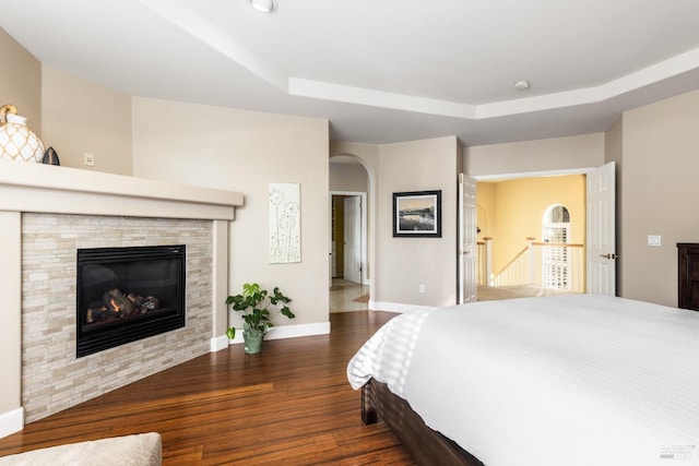 bedroom featuring a fireplace, dark hardwood / wood-style flooring, and a raised ceiling