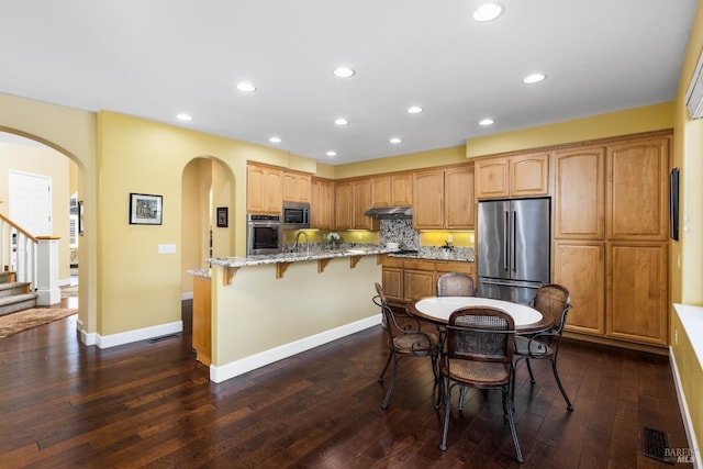 kitchen with light stone countertops, appliances with stainless steel finishes, a breakfast bar area, and dark hardwood / wood-style flooring