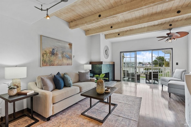 living area with a fireplace with raised hearth, ceiling fan, wood finished floors, wooden ceiling, and beamed ceiling