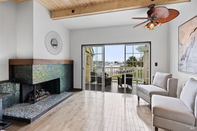 living room featuring a tile fireplace, hardwood / wood-style floors, beamed ceiling, ceiling fan, and wooden ceiling