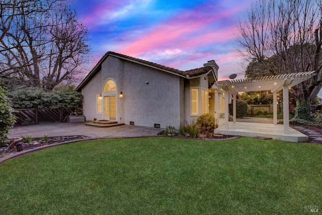 back house at dusk featuring a pergola, a lawn, and a patio