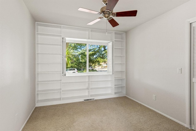 empty room with built in shelves, ceiling fan, and carpet flooring