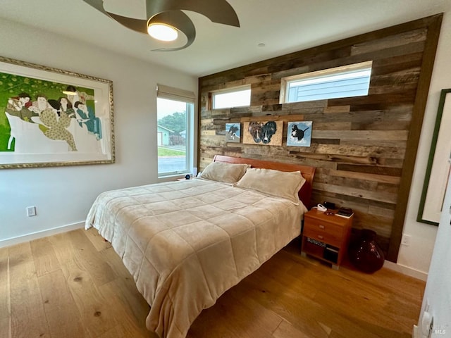 bedroom featuring ceiling fan, light hardwood / wood-style flooring, and wood walls