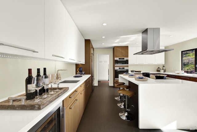 kitchen featuring a sink, island range hood, modern cabinets, light countertops, and recessed lighting