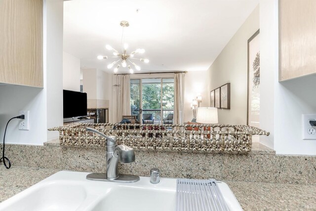 kitchen featuring light brown cabinetry, sink, light stone counters, and an inviting chandelier