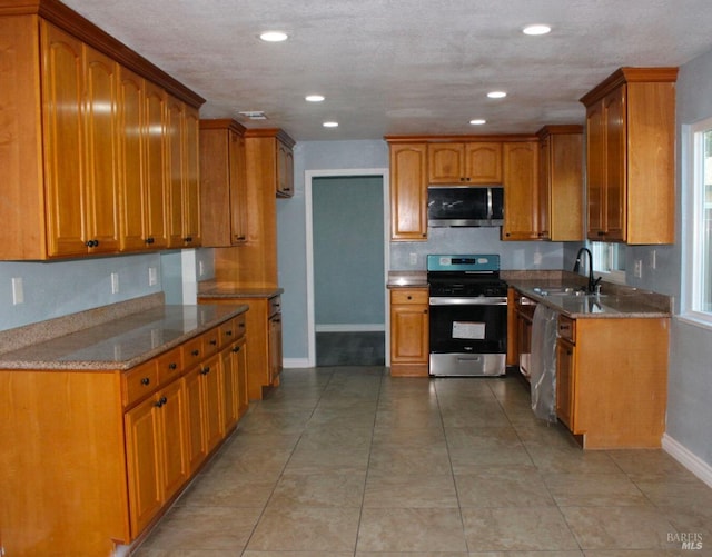 kitchen with stainless steel appliances, sink, light tile patterned floors, and stone counters