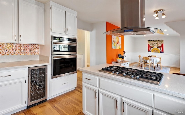 kitchen with stainless steel appliances, white cabinetry, island range hood, and beverage cooler