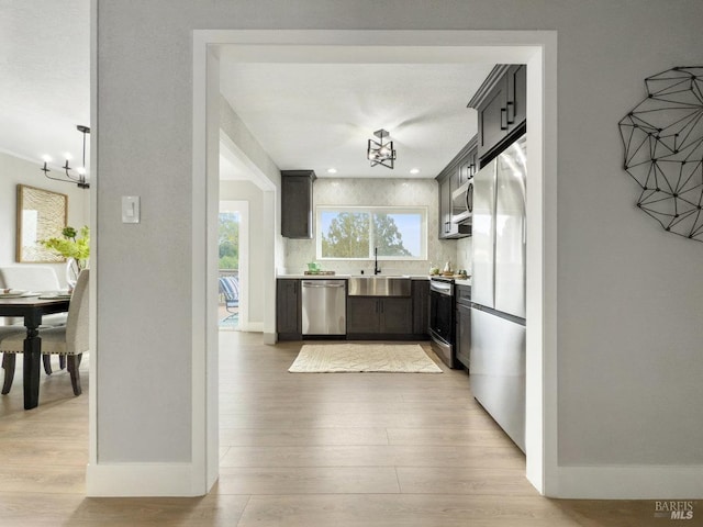 kitchen with sink, light wood-type flooring, a notable chandelier, stainless steel appliances, and backsplash