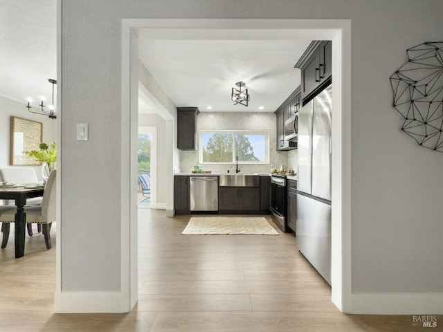 kitchen with a notable chandelier, a sink, backsplash, appliances with stainless steel finishes, and light wood-style floors