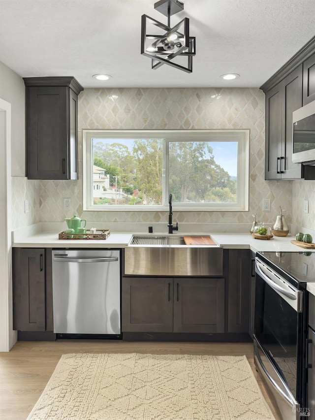 kitchen featuring light countertops, stainless steel appliances, a sink, light wood-type flooring, and backsplash