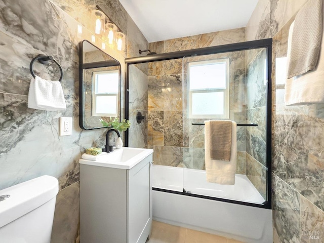 full bath with combined bath / shower with glass door, toilet, vanity, and tile walls