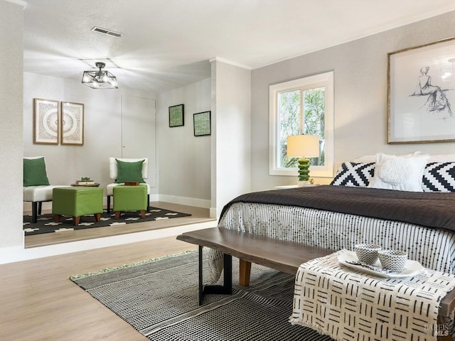 bedroom featuring baseboards, visible vents, wood finished floors, and ornamental molding