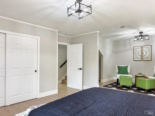 bedroom featuring crown molding, a chandelier, wood finished floors, a textured ceiling, and baseboards