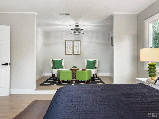 bedroom with baseboards, ornamental molding, visible vents, and wood finished floors