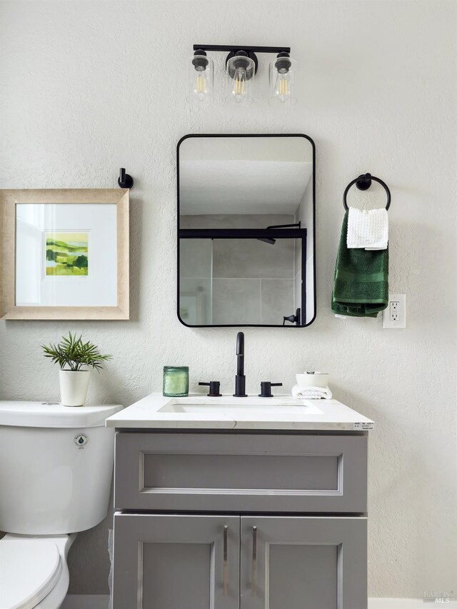 bathroom with a textured wall, toilet, and vanity