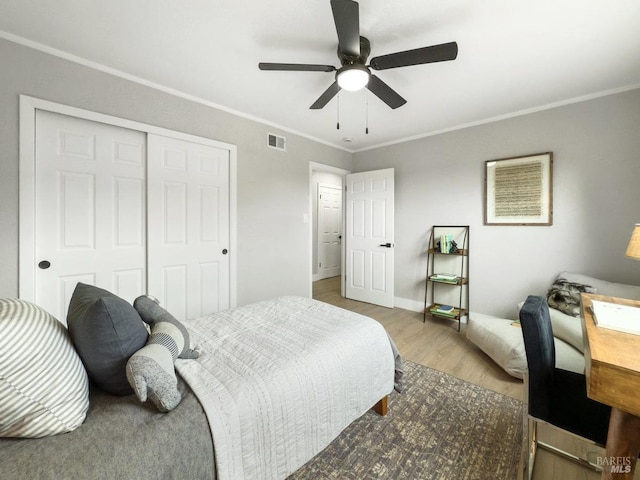 bedroom with a closet, visible vents, baseboards, ornamental molding, and wood finished floors