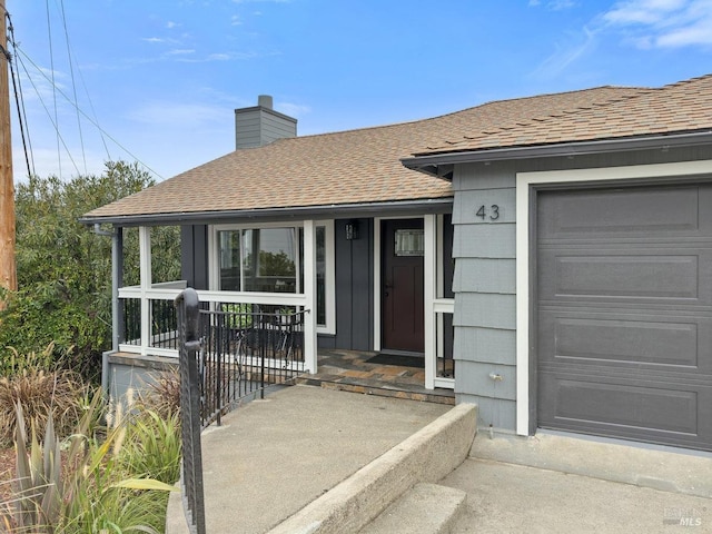 view of exterior entry featuring covered porch, a garage, a shingled roof, and a chimney