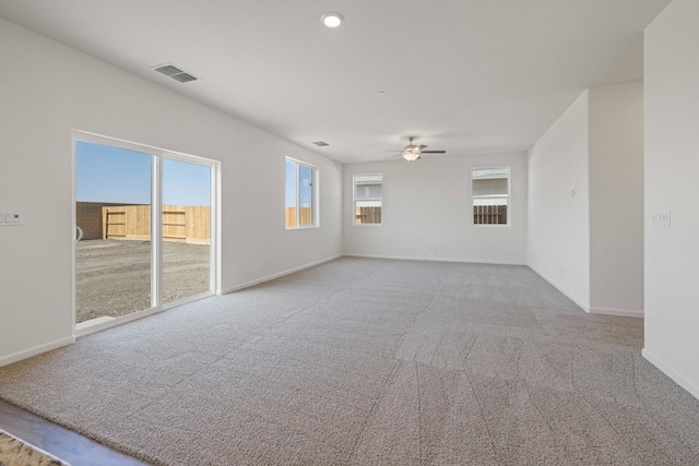 carpeted spare room featuring a ceiling fan, baseboards, visible vents, and a wealth of natural light