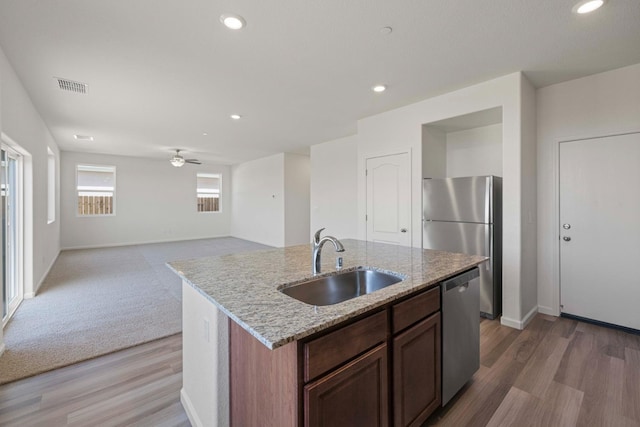 kitchen with appliances with stainless steel finishes, sink, ceiling fan, a center island with sink, and light hardwood / wood-style flooring