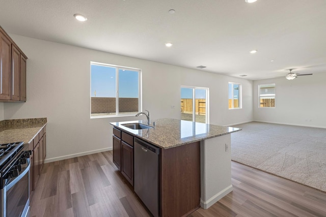 kitchen with sink, appliances with stainless steel finishes, hardwood / wood-style floors, light stone countertops, and a center island with sink