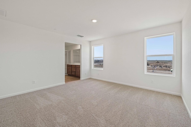 unfurnished bedroom with light carpet, visible vents, baseboards, and ensuite bathroom