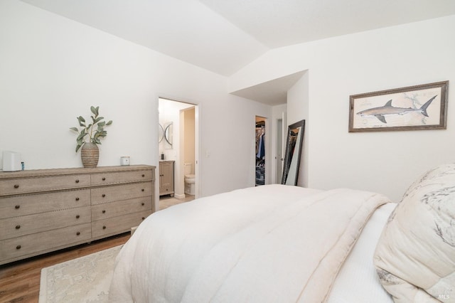 bedroom with connected bathroom, lofted ceiling, hardwood / wood-style flooring, a walk in closet, and a closet