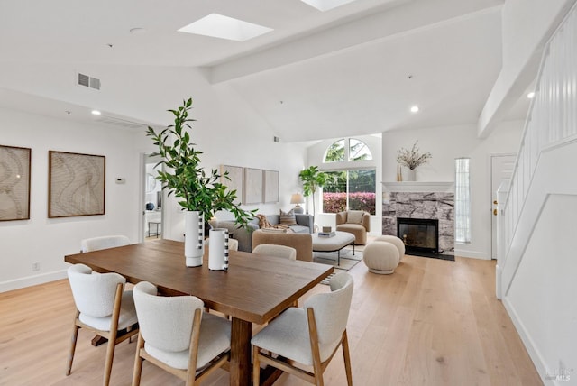 dining area with a premium fireplace, high vaulted ceiling, light hardwood / wood-style floors, and a skylight